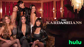Die Kardashian-Jenner Familie posiert gemeinsam in eleganten Abendkleidern auf einer Couch vor rotem Hintergrund.